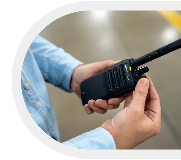 Motorola two-way radio being held by a person in a light-blue shirt.